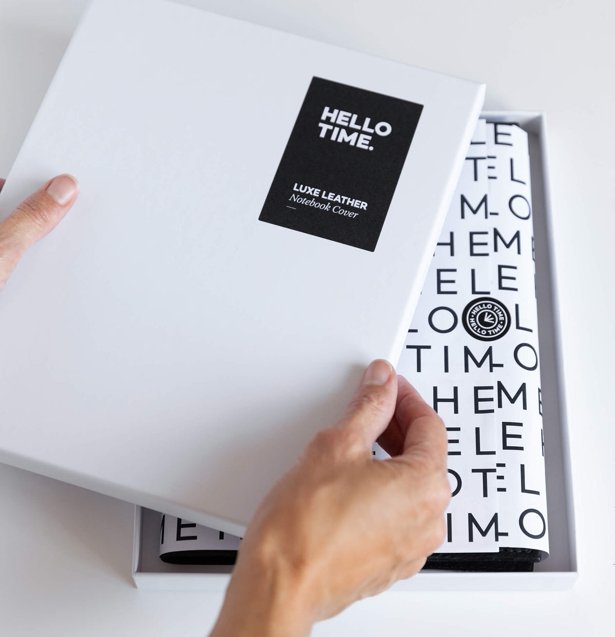 Hand opening white HELLO TIME "Luxe Leather Notebook Cover" box, branded tissue paper visible inside.