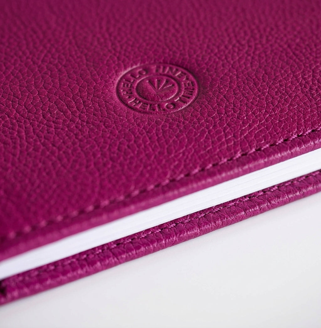 Close-up of magenta leather HELLO TIME notebook cover with embossed circular logo stamp.