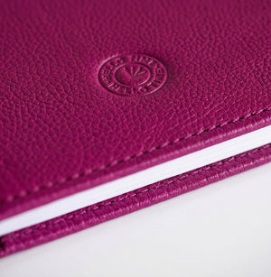 Close-up of magenta leather HELLO TIME notebook cover with embossed circular logo stamp.
