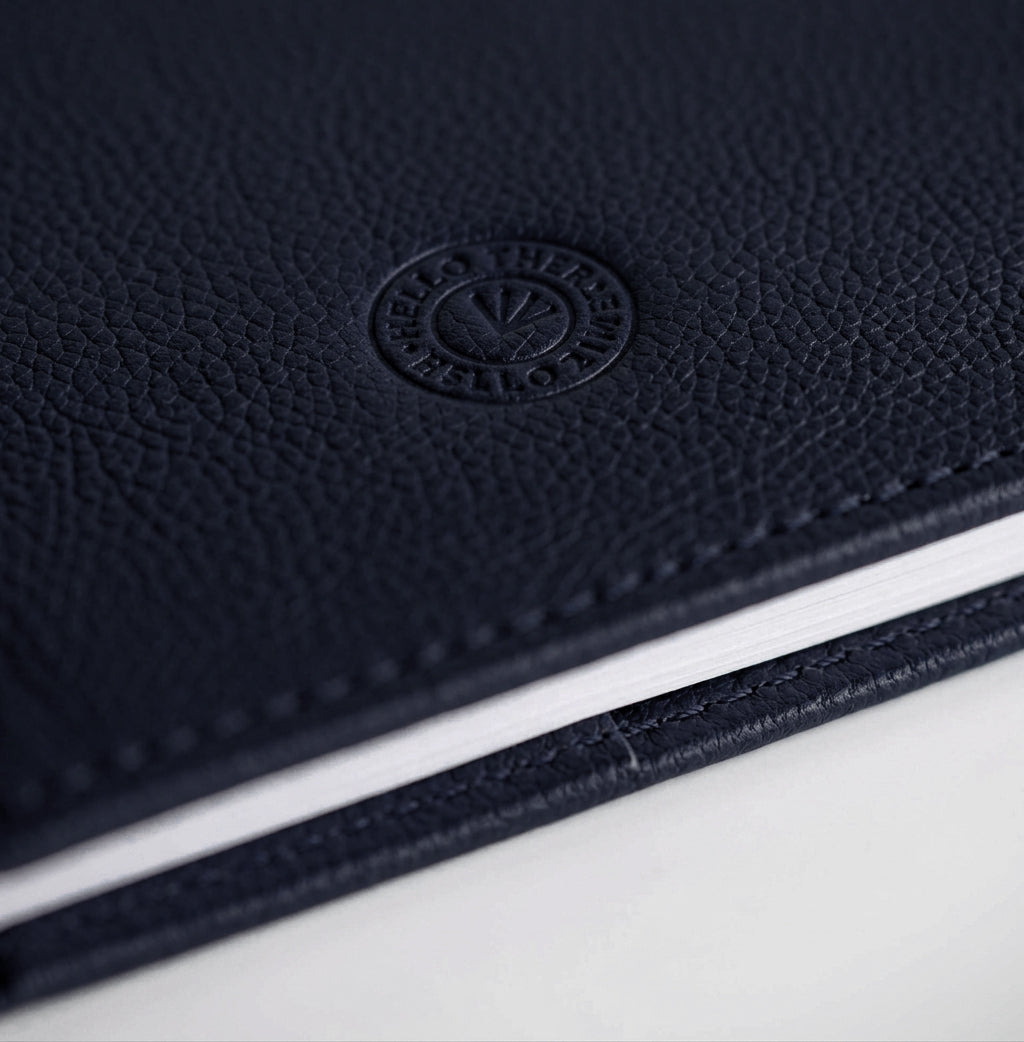 Close-up of navy leather HELLO TIME notebook cover with embossed circular logo stamp.