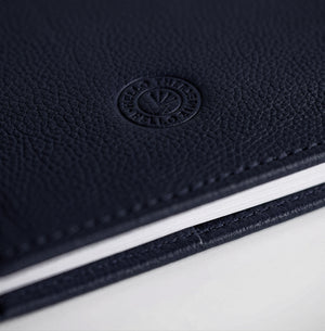 Close-up of navy leather HELLO TIME notebook cover with embossed circular logo stamp.