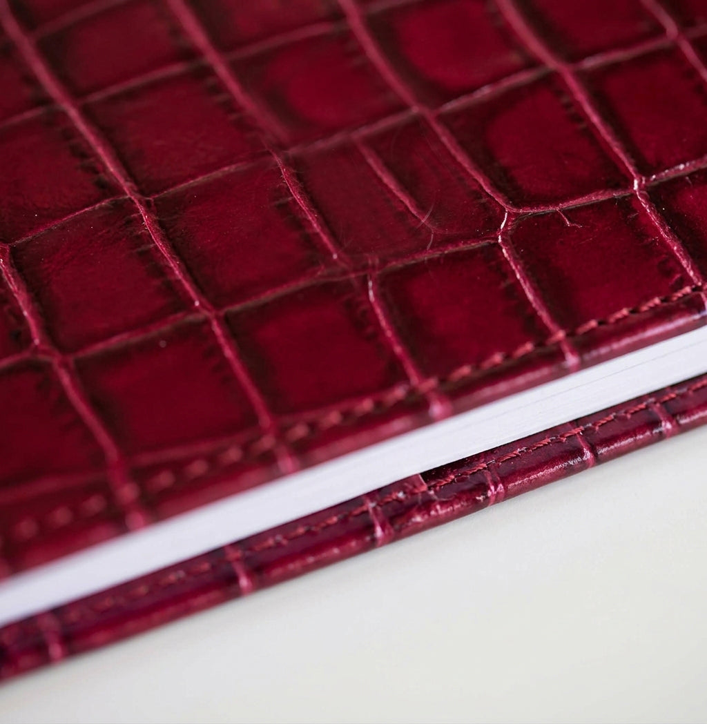 Close-up of dark red croc-embossed leather HELLO TIME notebook cover texture.