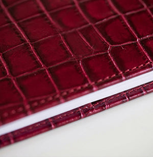 Close-up of dark red croc-embossed leather HELLO TIME notebook cover texture.