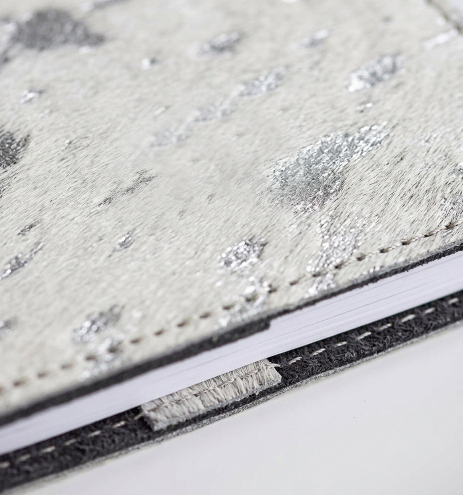 Close-up of white and silver metallic textured hair on hide HELLO TIME notebook cover, black trim edge.
