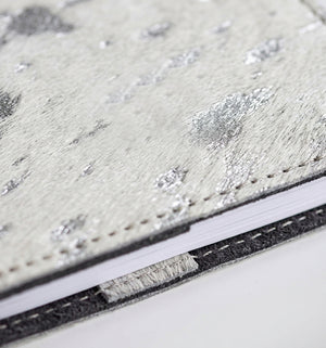 Close-up of white and silver metallic textured hair on hide HELLO TIME notebook cover, black trim edge.