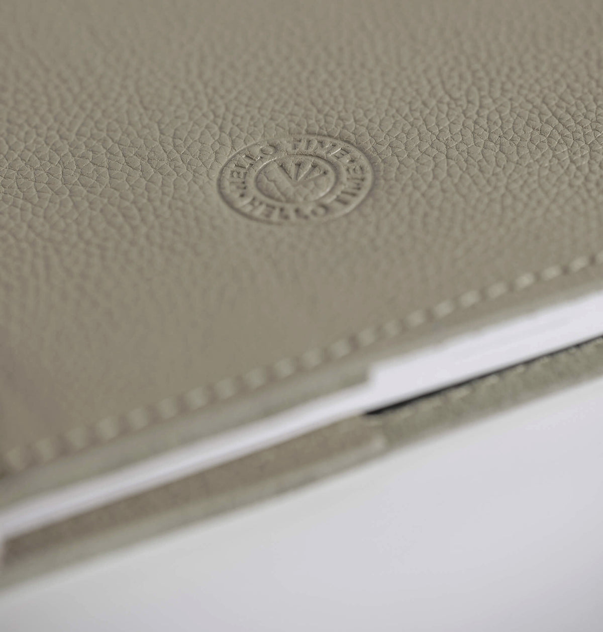 Close-up of beige leather HELLO TIME notebook cover with embossed circular logo stamp.