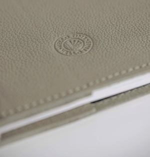 Close-up of beige leather HELLO TIME notebook cover with embossed circular logo stamp.