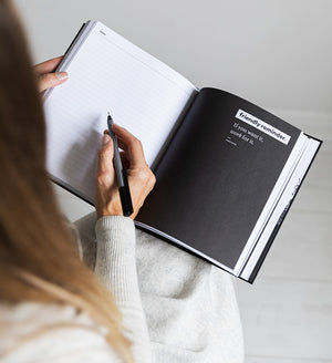 Person writing in HELLO TIME planner open to lined notes page with black quote page reading “If you want it, work for it”