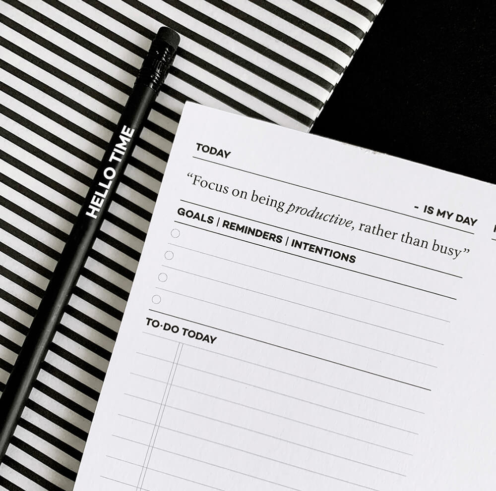Black HELLO TIME pencil and daily desk pad with quote and to-do list on striped background