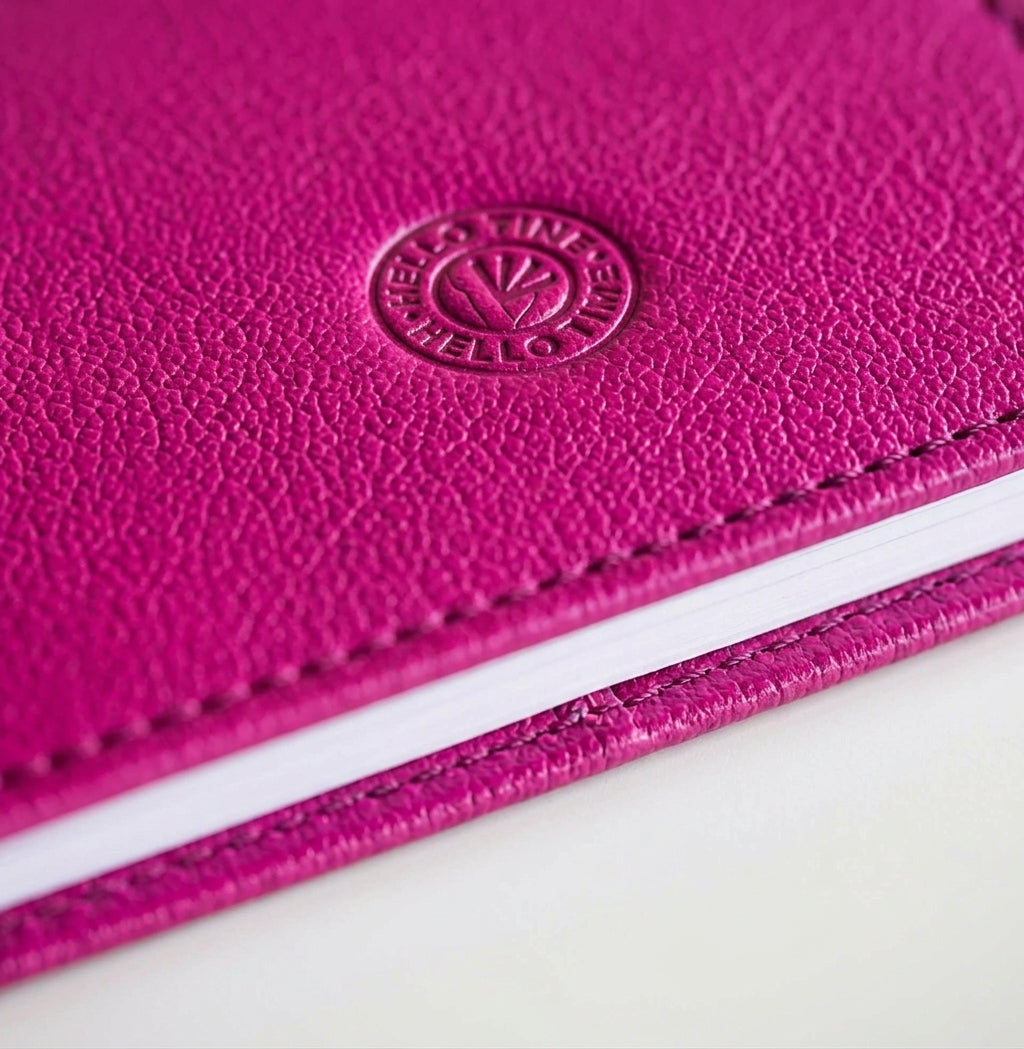 Close-up of pink leather HELLO TIME notebook cover with embossed circular logo stamp.
