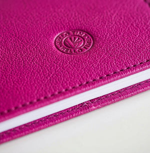 Close-up of pink leather HELLO TIME notebook cover with embossed circular logo stamp.