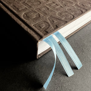 Close-up of brown HELLO TIME planner with embossed text and two pale blue ribbon bookmarks.
