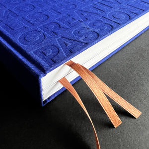 Close-up of blue HELLO TIME planner spine with embossed text and two caramel ribbon bookmarks.