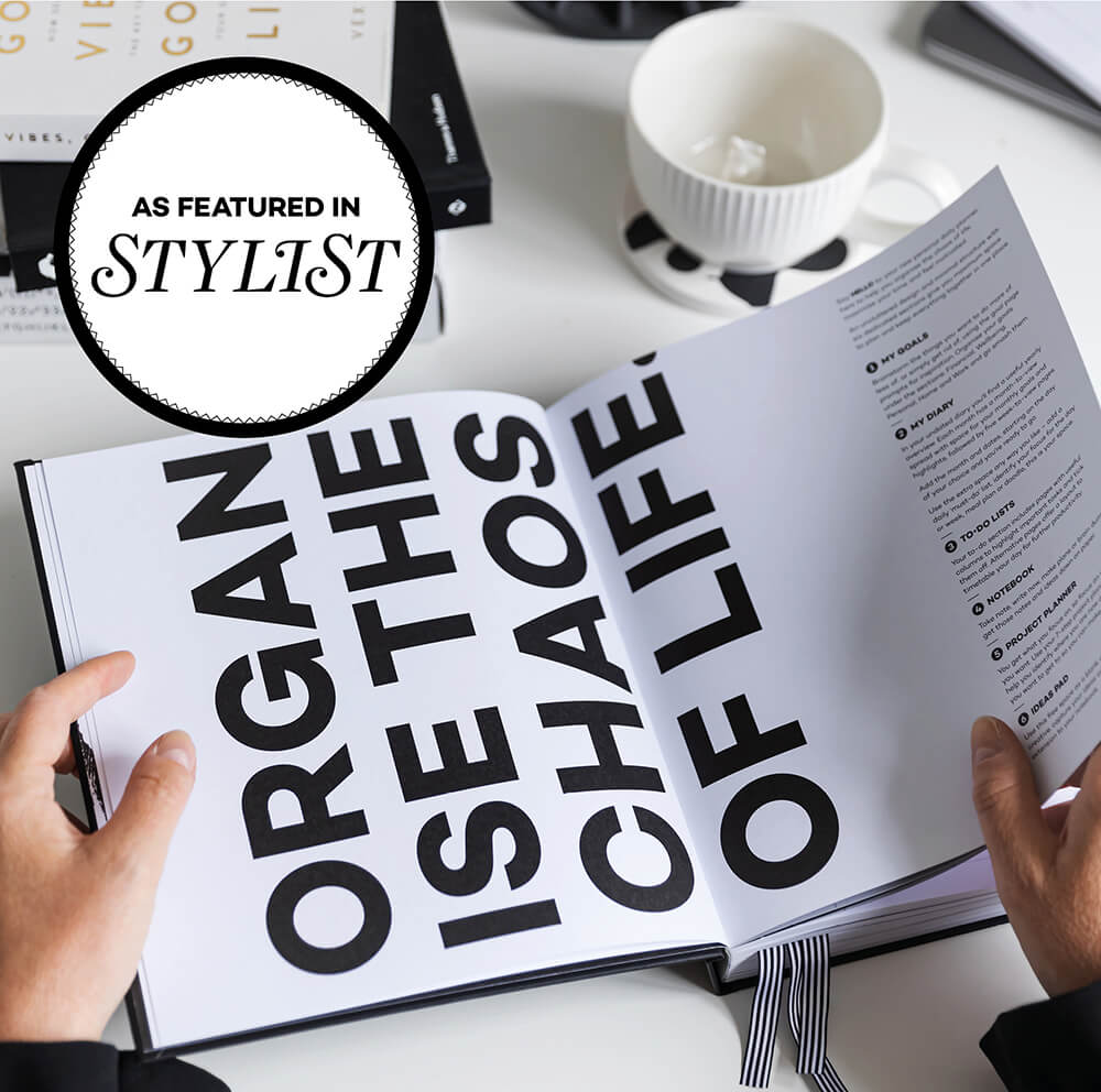 Woman holding black HELLO TIME undated planner and notebook with embossed words on cover