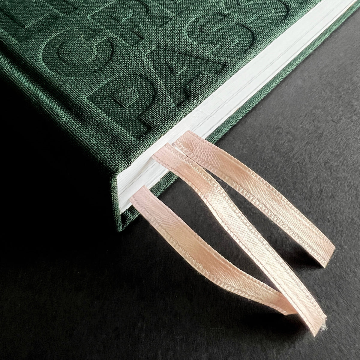 Close-up of green HELLO TIME planner spine with embossed text and two ribbon bookmarks threaded through the pages