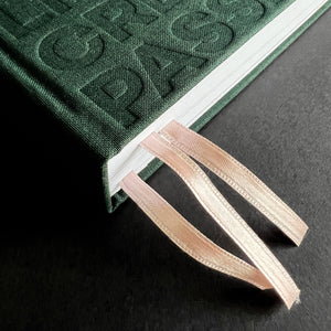 Close-up of green HELLO TIME planner spine with embossed text and two ribbon bookmarks threaded through the pages