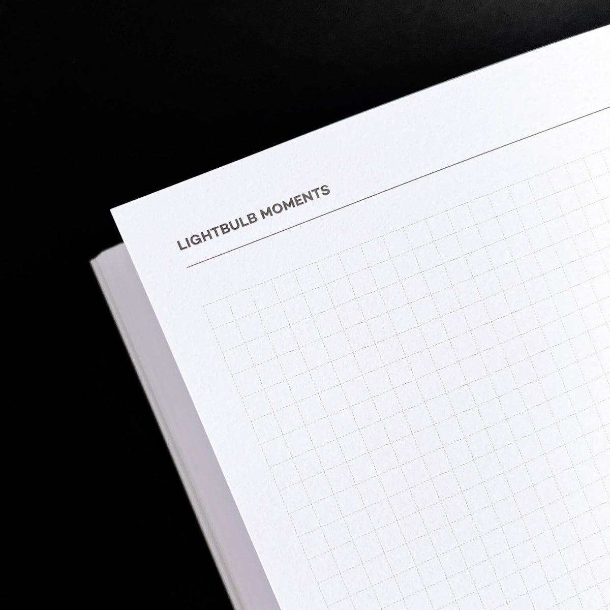 Open HELLO TIME planner "Lightbulb Moments" dotted grid page on black background, close-up angle.