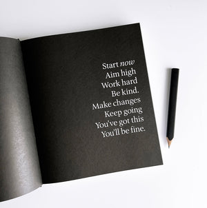 Open HELLO TIME planner showing black mantra page with white text beside a black pencil on white desk