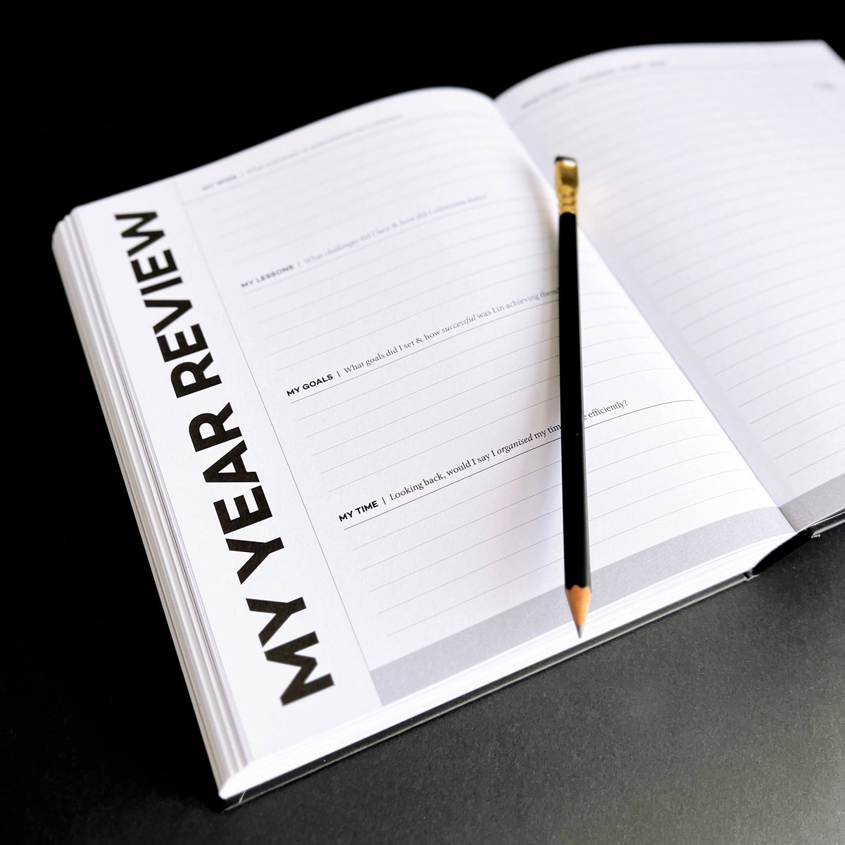 Open HELLO TIME "My Year Review" planner page with lined prompts for goals and lessons, pencil resting on top.