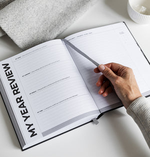Person turning striped ribbon in HELLO TIME planner open to “My Year Review” page with reflective prompts and lined sections
