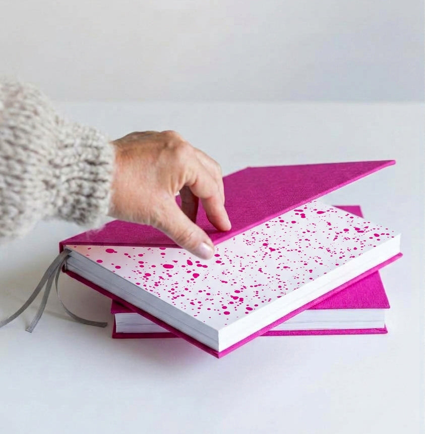 Hand lifting cover of pink HELLO TIME planner to reveal pink inkwell endpaper, taupe ribbon, second planner below.