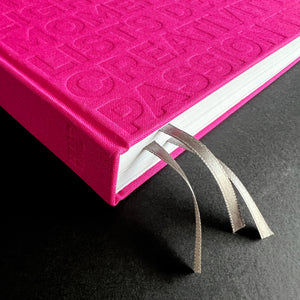Close-up of pink HELLO TIME planner spine with embossed text and two taupe ribbon bookmarks.