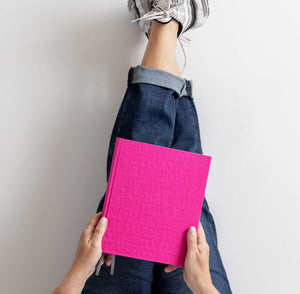Person lying back with feet up a wall, holding closed pink HELLO TIME planner with embossed cover text on their lap.