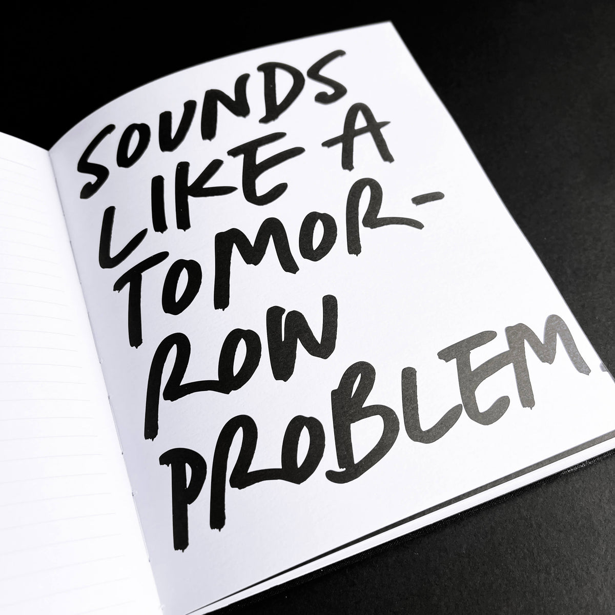 Open HELLO TIME notebook page with handwritten "Sounds like a tomorrow problem" quote on black background.