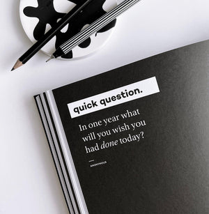 Black HELLO TIME planner page with bold white quote and pencils on white desk