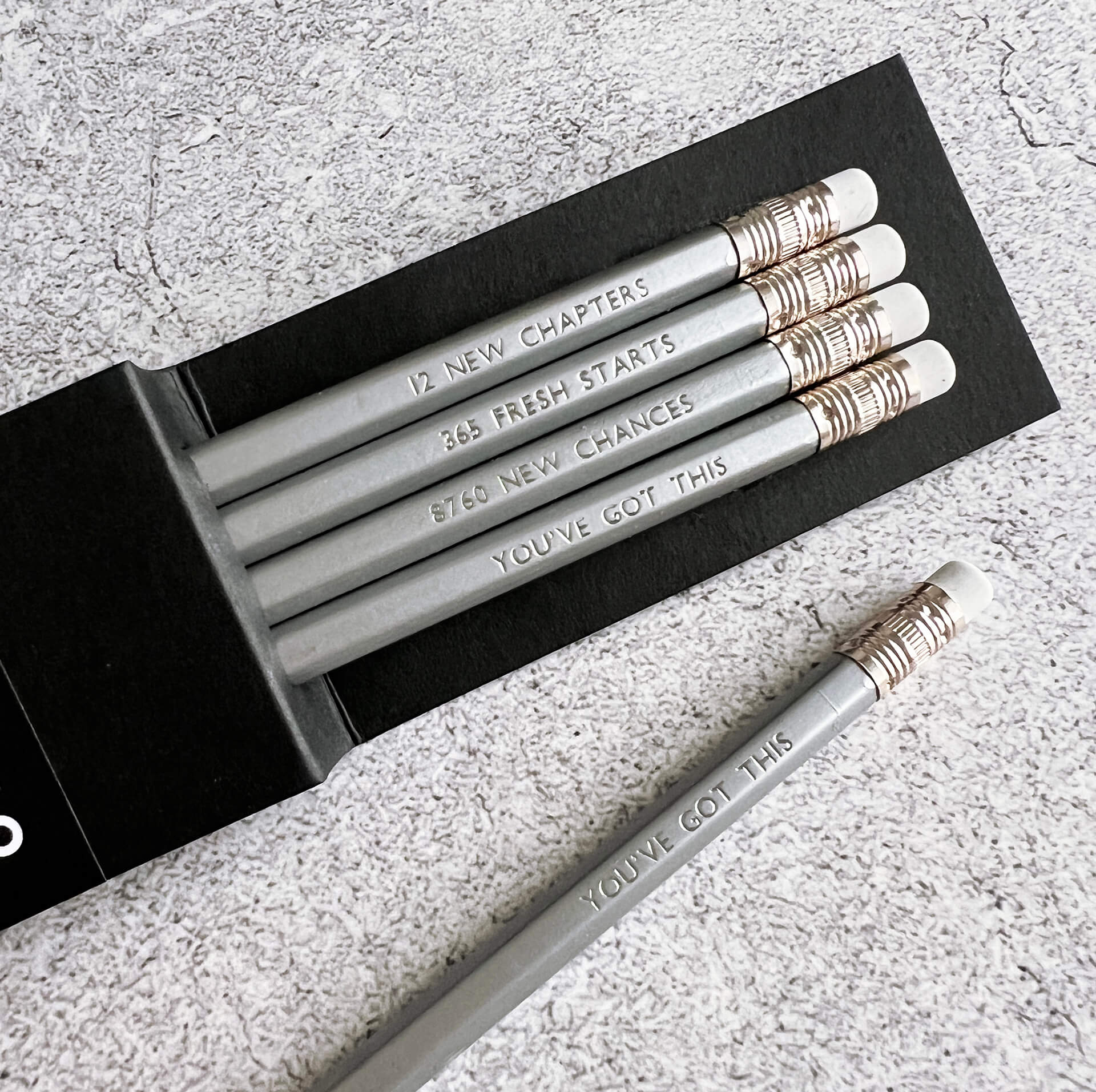 HELLO TIME silver pencils with motivational time quotes and white erasers in black sleeve on grey textured background