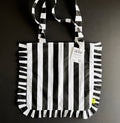 Black and white striped HELLO TIME tote bag with ruffled edges, laid flat with branded tag attached