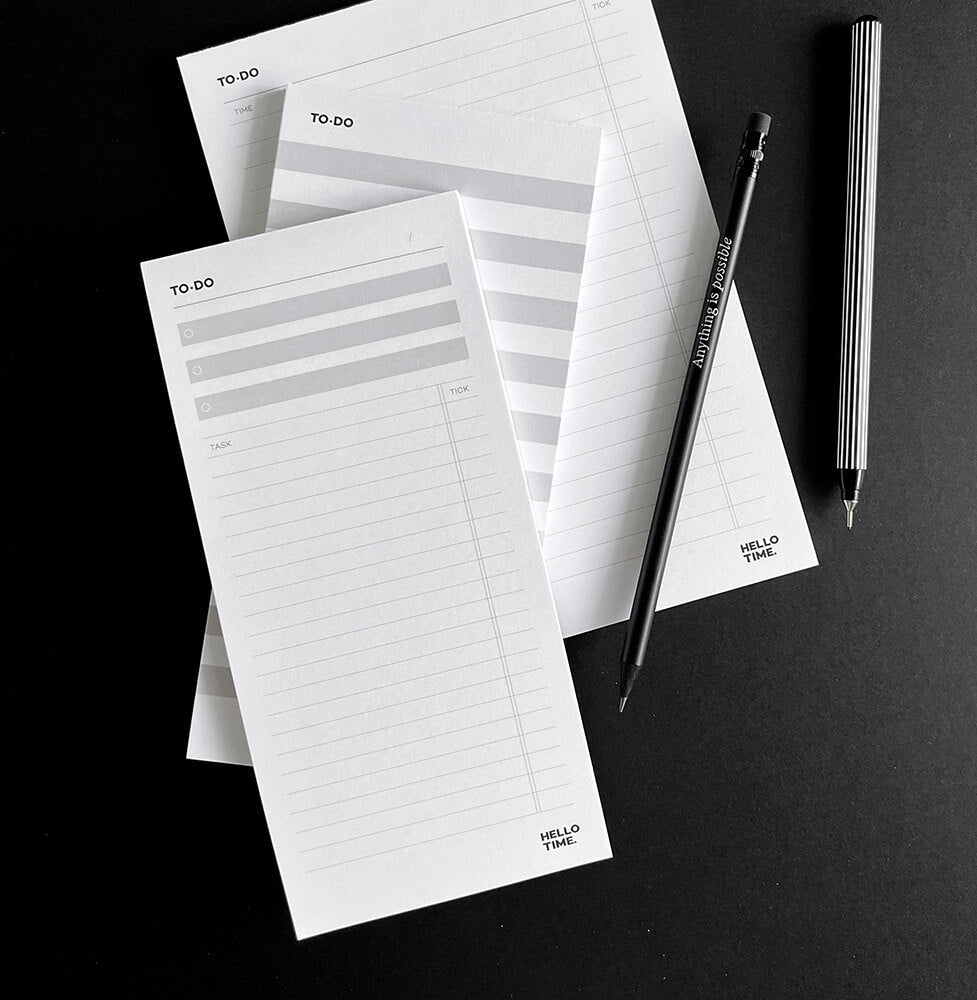 Flat lay of HELLO TIME desk pads including Top 3, Braindump, and Time Task Tick with black pencil and pen on black background