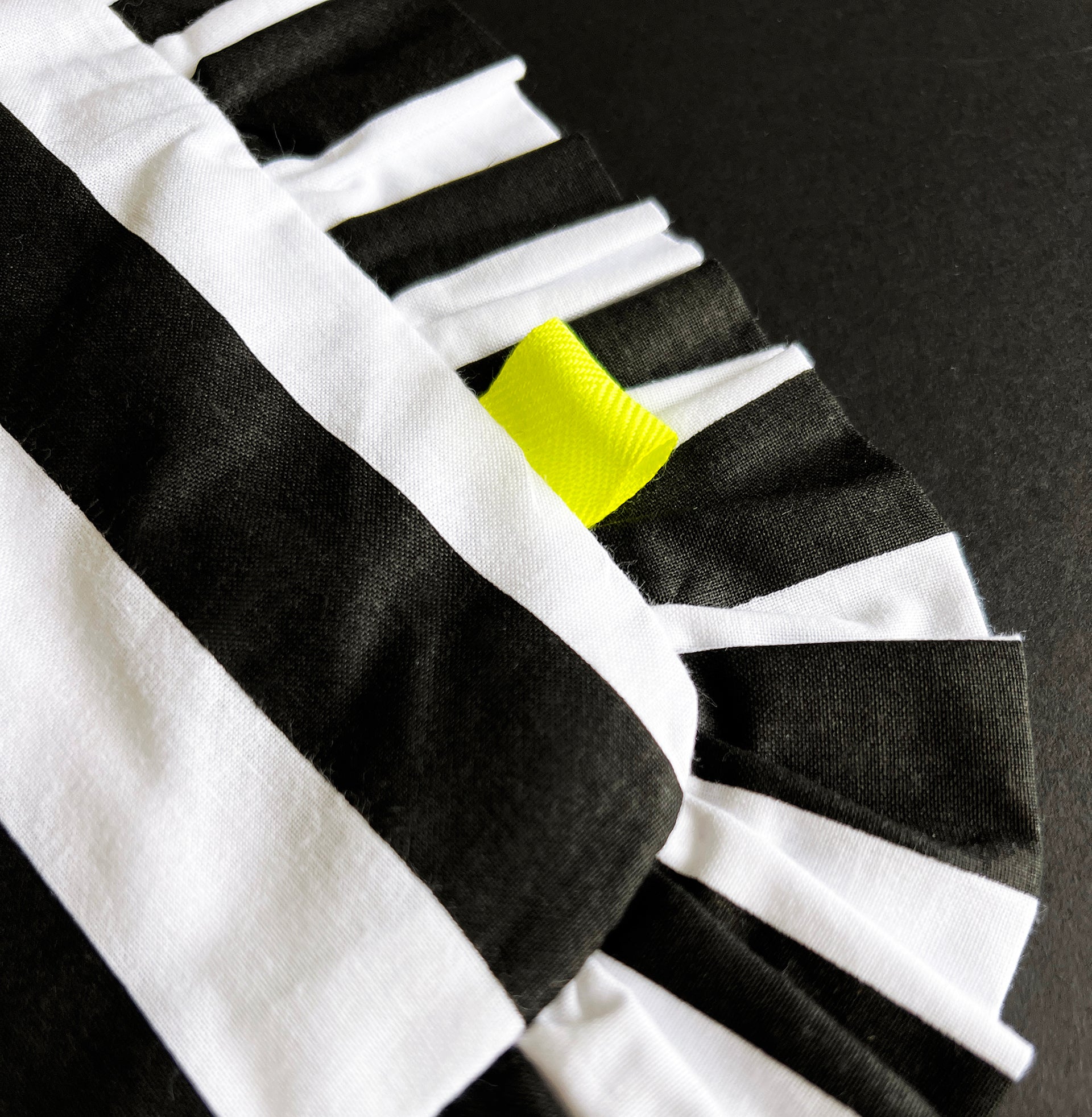 Close-up of black and white striped HELLO TIME tote bag with neon yellow tab and pleated edge.