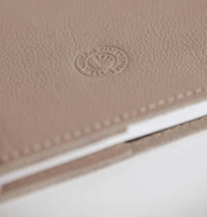 Close-up of warm cream leather HELLO TIME notebook cover with embossed circular logo stamp.