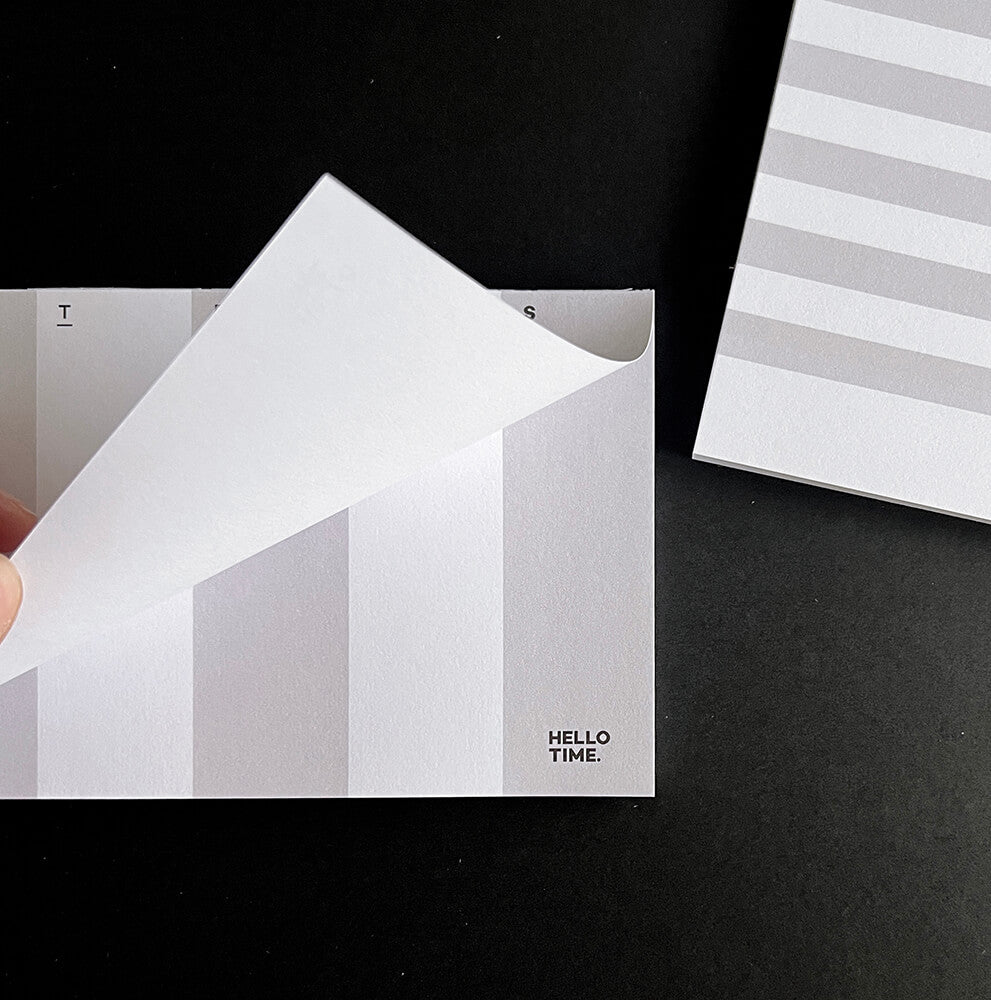 Close-up of HELLO TIME DL weekly pad with a page being turned, showing pale columns for each day of the week.