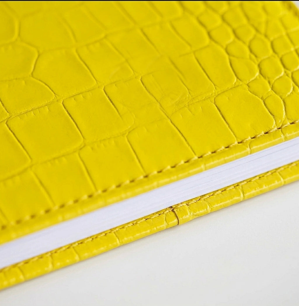 Close-up of yellow croc-embossed leather HELLO TIME notebook cover texture.