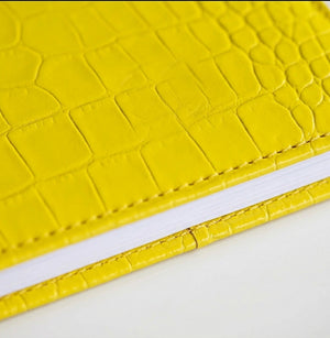 Close-up of yellow croc-embossed leather HELLO TIME notebook cover texture.