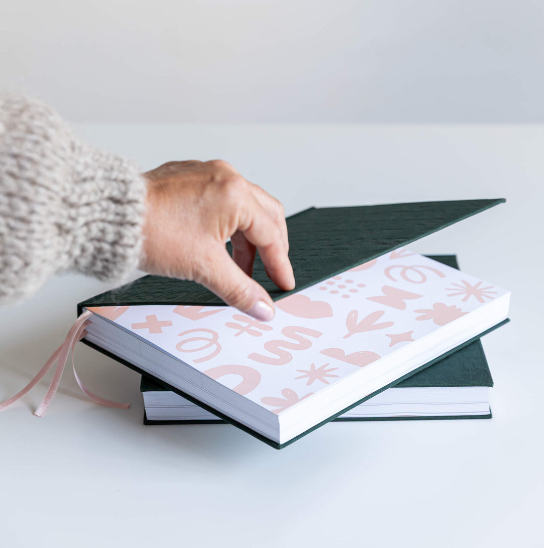 Smiling woman in glasses holding open green HELLO TIME planner showing embossed text on front and back covers.
