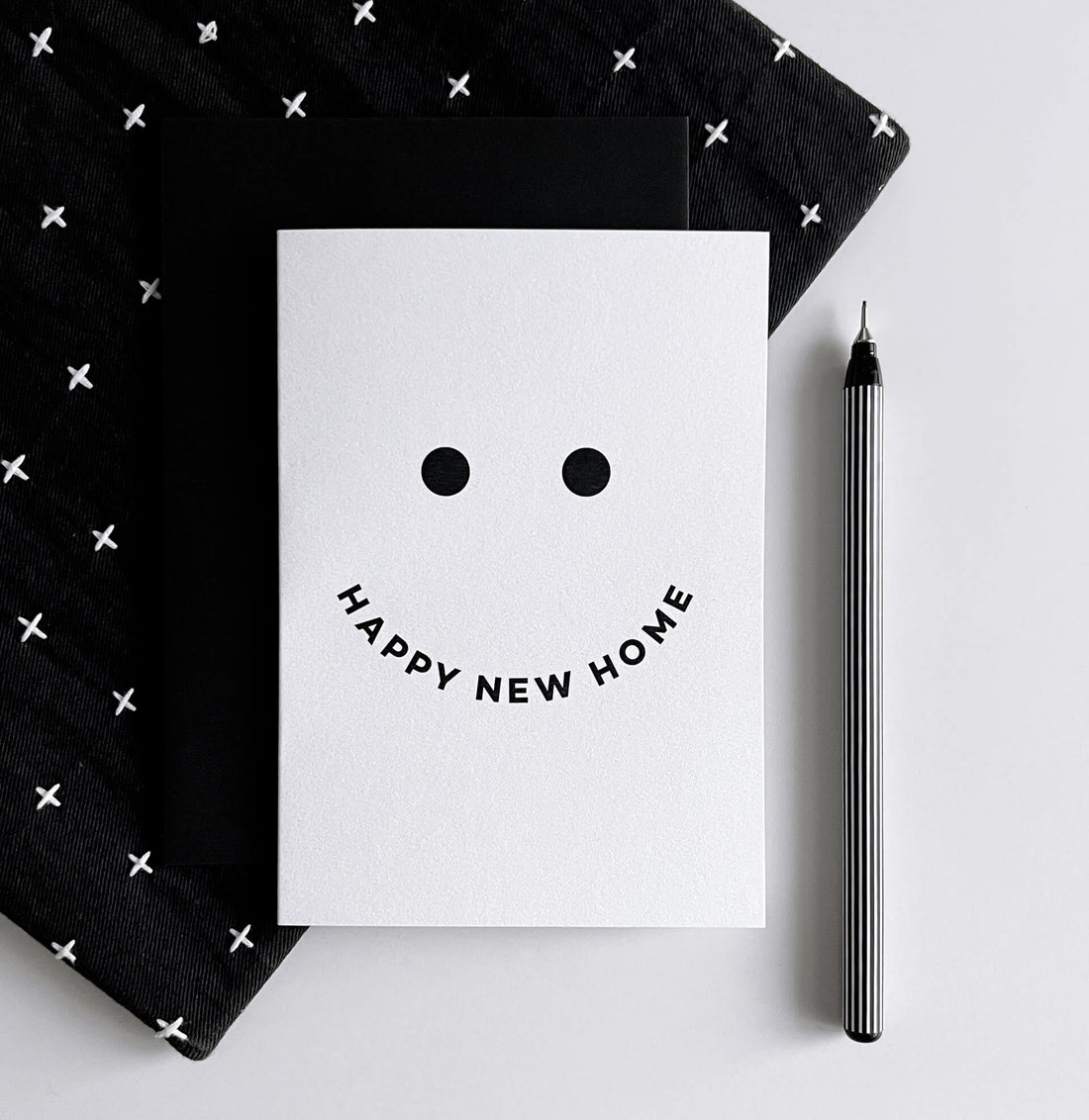 White card with black smiley face design and curved text “Happy New Home,”. 