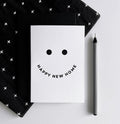 White card with black smiley face design and curved text “Happy New Home,”. 