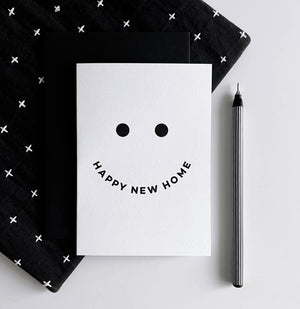 White card with black smiley face design and curved text “Happy New Home,”. 