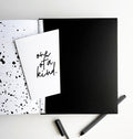 Planner open to black pocket with “one of a kind” greetings card and striped black fineliner pen
