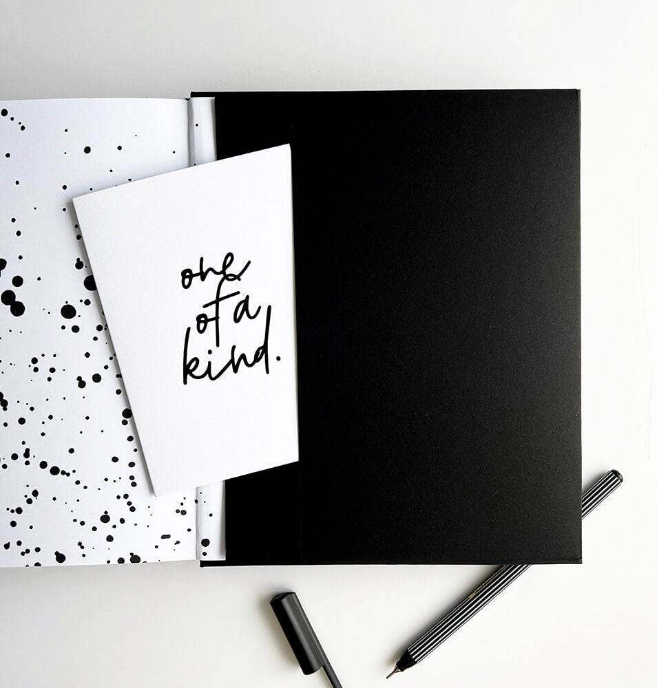 Planner open to black pocket with “one of a kind” greetings card and striped black fineliner pen
