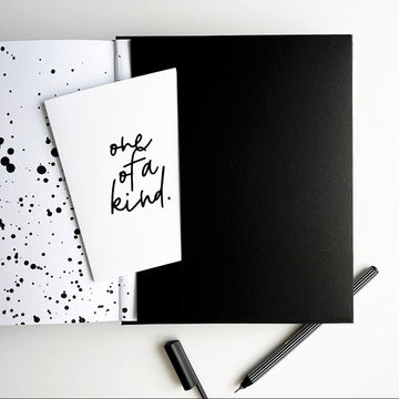 Planner open to black pocket with “one of a kind” greetings card and striped black fineliner pen
