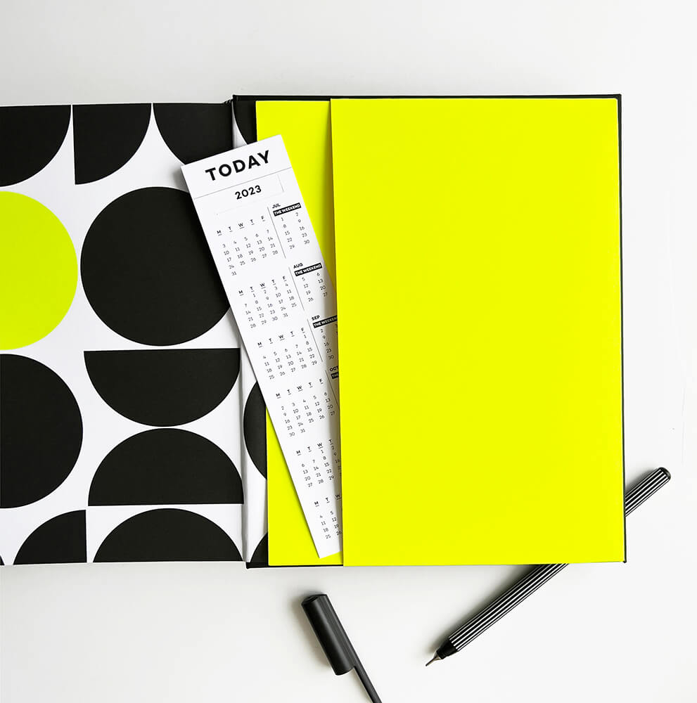 Open planner showing neon yellow pocket, calendar bookmark and black pen with striped barrel