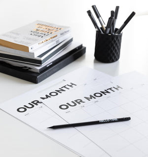 Two monthly Hello Time wall planner sheets on white desk with pencil and pens