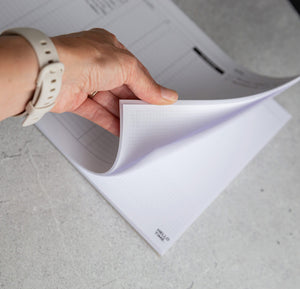Person flipping through Hello Time My Week Desk Pad showing dot grid and weekly layout on grey surface