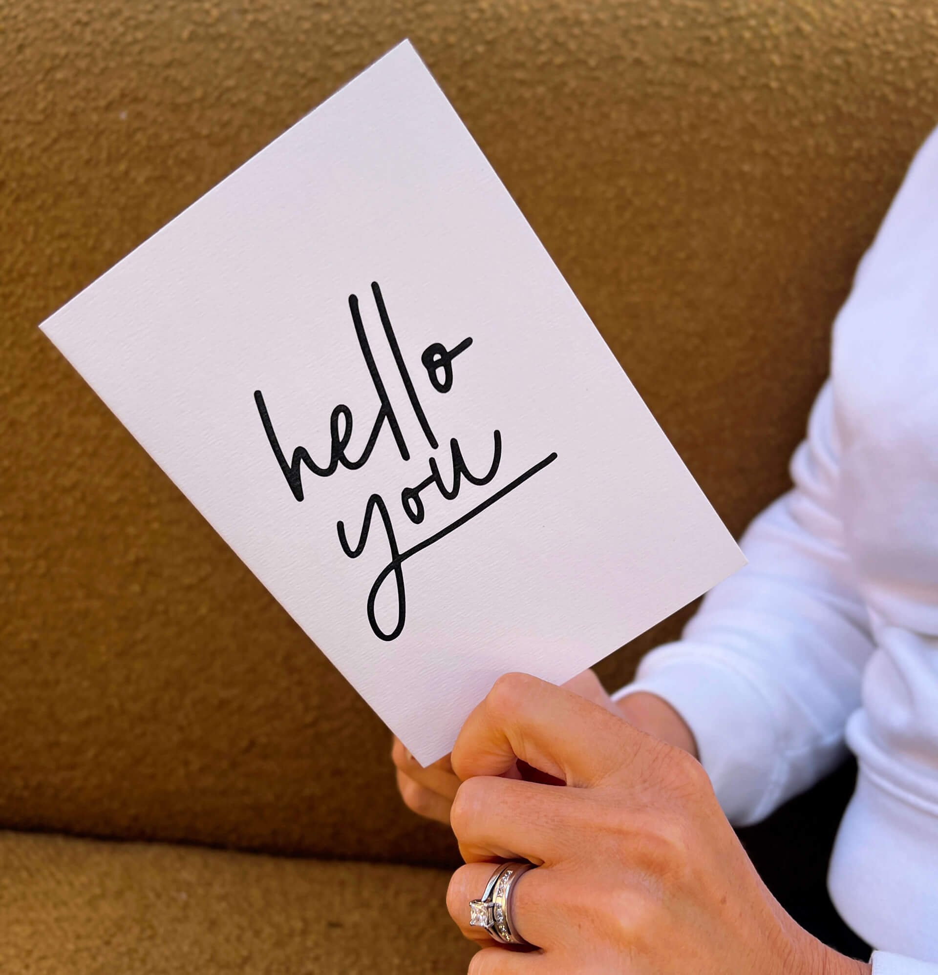 Person holding white friendship card with black text “hello you” on the front.