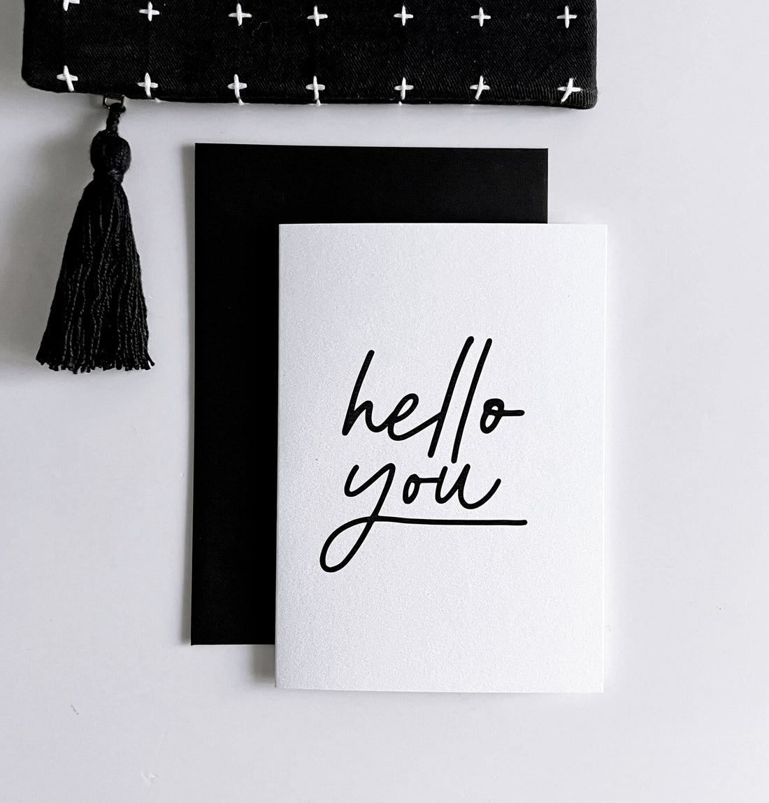 White friendship card with black handwritten text “hello you,” shown with black envelope.
