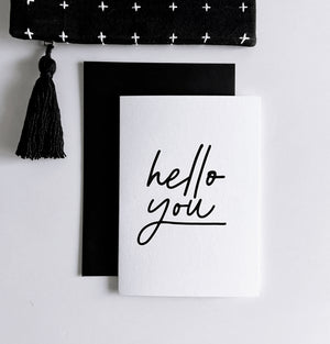 White friendship card with black handwritten text “hello you,” shown with black envelope.